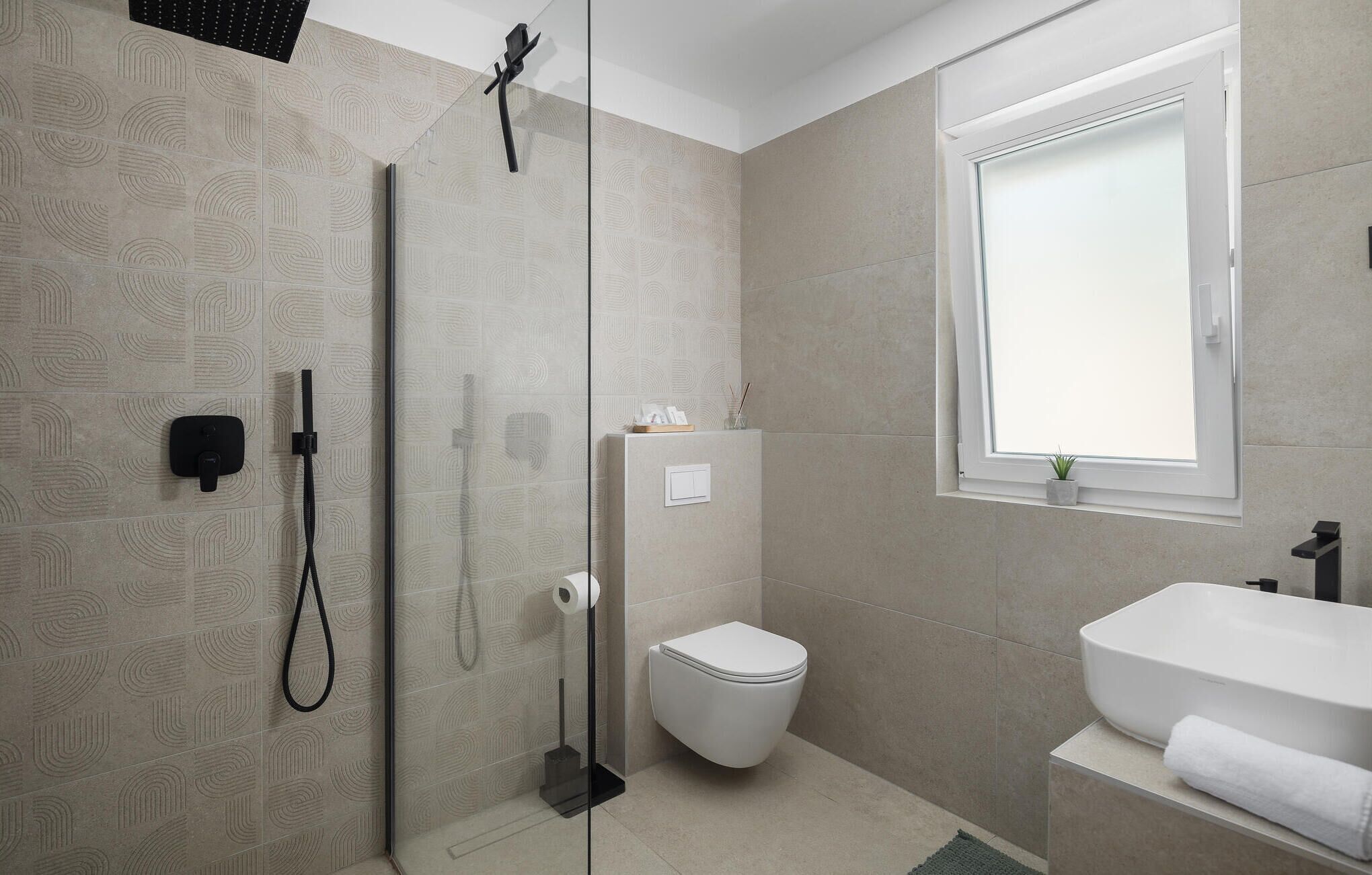 A modern bathroom with a glass shower enclosure, a toilet, and a sink with a towel.