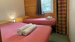 Una cabaña con dos camas, cada una con una colcha rosa y toallas enrolladas, paredes de madera, una ventana con cortinas y una alfombra verde.