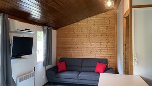 Una habitación acogedora con techo de madera, un sofá gris con cojines rojos, un televisor de pantalla plana y una mesa blanca.