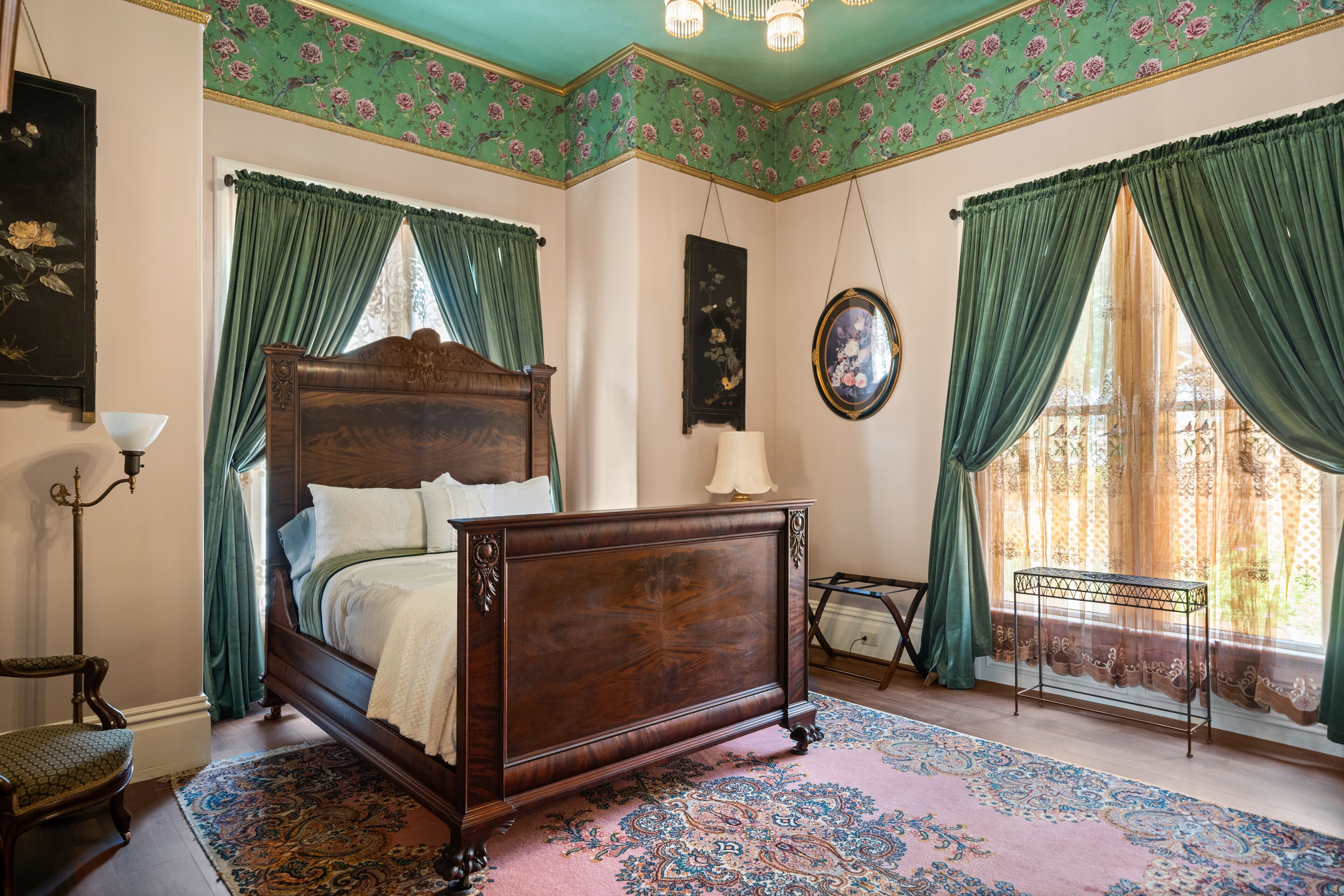 A bedroom with a wooden bed, green curtains, a patterned rug, and a small table.