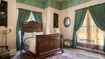A bedroom with a wooden bed, green curtains, a patterned rug, and a small table.
