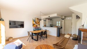A spacious living area with a dining table, a lounge chair, and a TV mounted on the wall. - PORT GRIMAUD Renovated South-oriented house - A/C, WIFI, 11m mooring (Grimaud)
