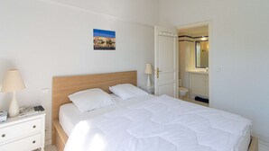 A neatly made bed with white bedding, a bedside table with a lamp, and a small painting on the wall. - PORT GRIMAUD Renovated South-oriented house - A/C, WIFI, 11m mooring (Grimaud)