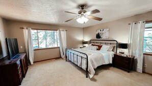 Un dormitorio con cama, ventilador de techo, ventana con cortinas, cómoda y televisor.