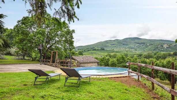 A pool area with two lounge chairs, a wooden fence, and a view of green hills in the background.