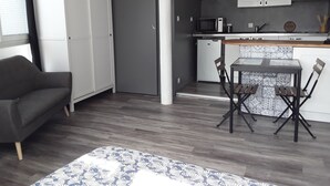 A compact living space with a kitchenette, a dining area with a table and chairs, and a sofa. - Studio lumineux proche de la mer (Saint-Nazaire)