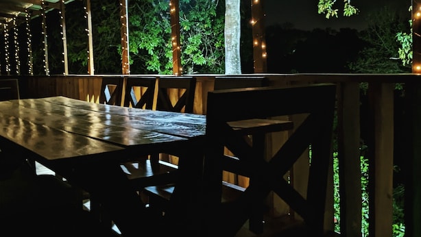 Un espace extérieur aménagé pour les repas, avec une table et des chaises en bois, entouré d’une balustrade en bois.