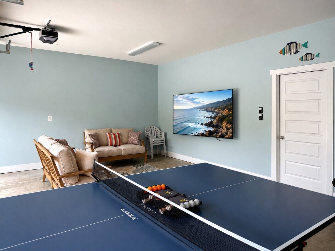 Ein Tischtennistisch in einem Raum mit hellblauer Wand, einer Couch und einem Gemälde einer Küstenlandschaft.