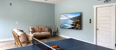 Ein Tischtennistisch in einem Raum mit hellblauer Wand, einer Couch und einem Gemälde einer Küstenlandschaft.