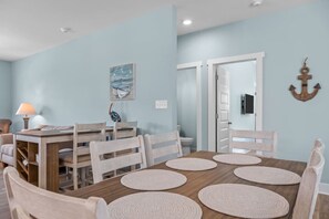 A dining area with a wooden table and chairs, a lamp, and a painting on the wall. - Modern Beach Villa|2-Min Walk to Beach + Ping Pong (Emerald Isle)