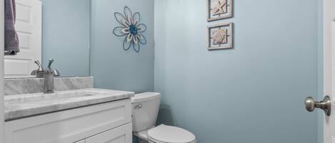 A bathroom with a white vanity, a sink, a toilet, and a blue wall.