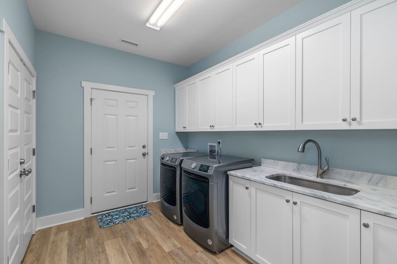 A kitchen with white cabinets, a stainless steel sink, and two built-in ovens.