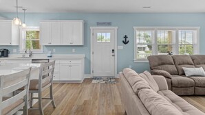A modern kitchen with white cabinets, a dining area with a white table and chairs, and a living room with a beige sofa. - Modern Beach Villa|2-Min Walk to Beach + Ping Pong (Emerald Isle)
