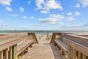 Pasarela de madera que conduce a una playa con vistas claras al océano y al cielo.