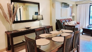 Un coin repas avec une table en verre, des chaises en bois, un vase contenant de l’herbe des pampas, un bol de collations et une lampe.