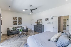 Un dormitorio amplio con una cama grande, un sofá, un aparador y un ventilador de techo.