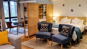 A hotel room with a bed, two armchairs, a sofa, a wooden bookshelf, and a dining area with a table and chairs. - Ruru Studio (Auckland)