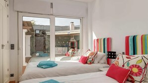 Un dormitorio con dos camas, un balcón y vista a un edificio de fachada de piedra.