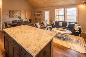 Una cocina amplia con una isla de granito, armarios de madera y un comedor con sillas.