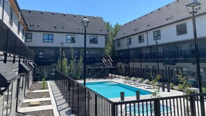 A modern hotel courtyard with a swimming pool, outdoor seating, and a staircase leading to the upper floors. - Enchanted Mountain Getaway: Accessible Retreat in Canmore, Close to Banff (Canmore)
