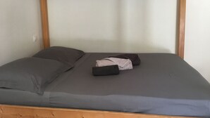 A single bed with a grey mattress and pillows, wooden headboard, and a simple white wall. - Studio Proche Mer/montagne, Lieu Calme et Convivial (Santa-Maria-Poggio)