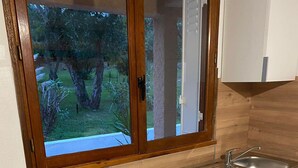 A compact kitchen with a built-in microwave, a sink, and a window overlooking a garden. - Studio Proche Mer/montagne, Lieu Calme et Convivial (Santa-Maria-Poggio)