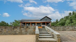 A stone-walled building with a covered porch and a staircase leading to a wooden deck. - Sip, Fish & Relax Fireside: Serene Schulenburg Gem (Schulenburg)