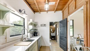 A modern kitchen with white cabinets, a wooden ceiling, and a view through an open door to a dining area. - Sip, Fish & Relax Fireside: Serene Schulenburg Gem (Schulenburg)