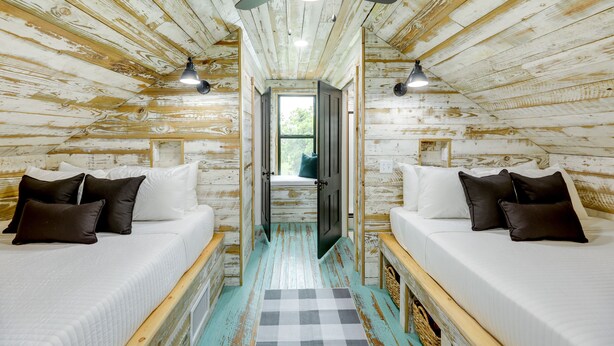 A rustic wooden room with two beds, a checkered rug, and a ceiling fan. - Sip, Fish & Relax Fireside: Serene Schulenburg Gem (Schulenburg)