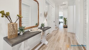 Ein Flur mit einem dunklen Holzkonsole, einem großen Spiegel und einer weißen Tür. Auf der Konsole stehen Blumentöpfe und eine Vase mit getrockneten Blumen.