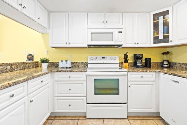 A kitchen with white cabinets, a white stove, a microwave, and a coffee maker. - Beautiful ground floor condo. Steps to the heated pool, BBQ grills, and beach! ☀️ (Cocoa Beach)