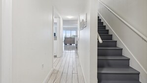 A hallway with white walls, a wooden floor, and a staircase with dark steps. - Ocean View Condo Close to the Pier on the Beach! (Cocoa Beach)