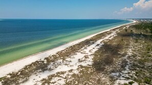 A beach with clear water, a sandy shore, and sparse vegetation.