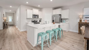 Una cocina moderna con armarios blancos, electrodomésticos de acero inoxidable y taburetes de bar color turquesa.