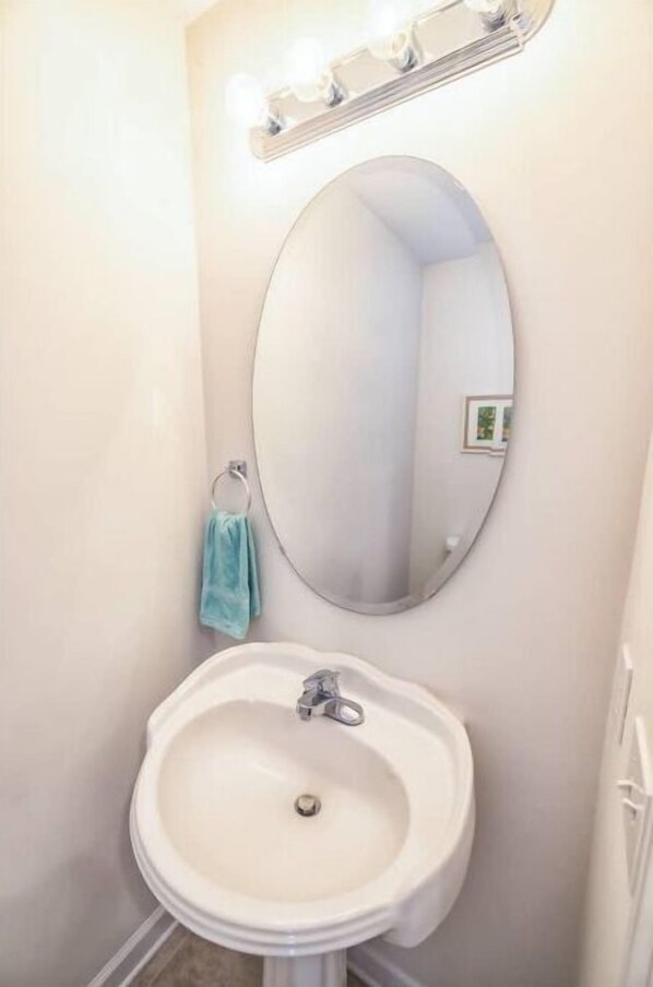 A bathroom with a white sink, a round mirror, and a lighted vanity mirror.