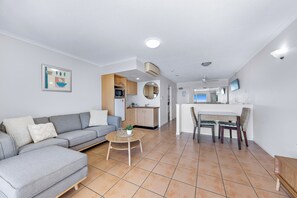 A modern living room with a grey sofa, a round coffee table, and a kitchen area in the background. - Shingley Ocean Views (Cannonvale)
