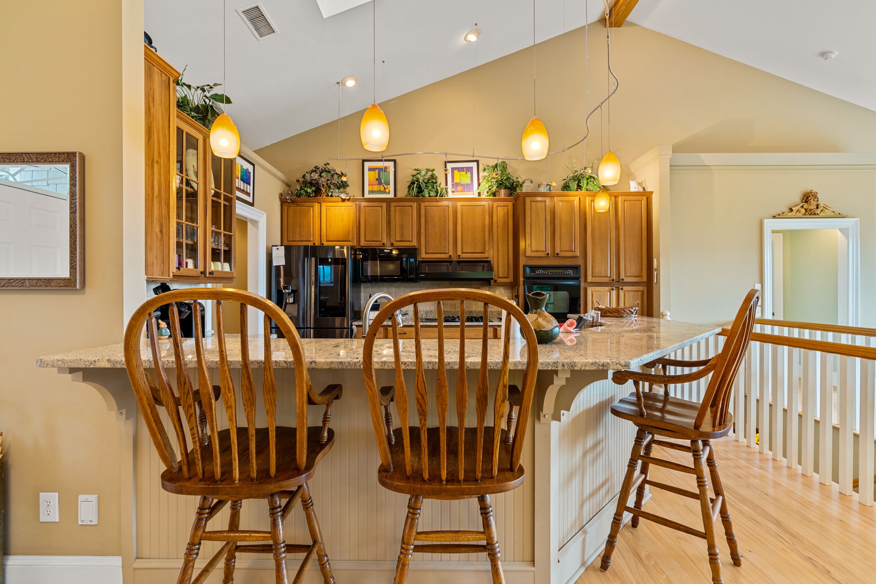 A kitchen with wooden cabinets, a central island with bar stools, pendant lighting, and a view of the living area.