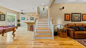 Un espacio habitable amplio con una escalera de madera, una mesa de billar y un sofá de cuero marrón.