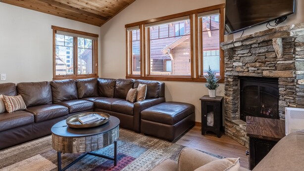 A cozy living room with a stone fireplace, leather sofa, and large windows.
