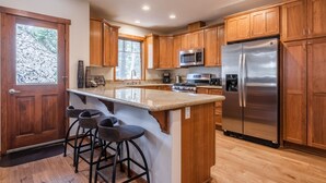 A modern kitchen with wooden cabinets, stainless steel appliances, and a bar area with stools.
