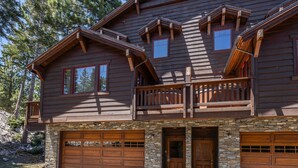 A two-story log cabin with a stone foundation, a balcony, and two garage doors.