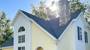A two-story house with a stone chimney, a yellow exterior, and a front door with a small porch. - Tranquility in Downtown Fish Creek (Fish Creek)
