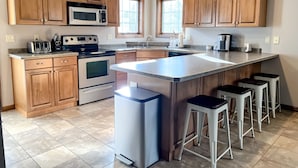 A modern kitchen with wooden cabinets, stainless steel appliances, and a large island with bar stools. - Tranquility in Downtown Fish Creek (Fish Creek)