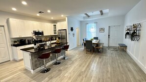 A modern kitchen with white cabinets, a central island with bar stools, and a dining area with a table and chairs. - Gorgeous Pool House in North Port, FL (North Port)