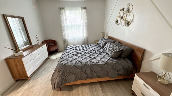 Une chambre moderne avec un lit en bois, une commode, une chaise et un élément décoratif mural.