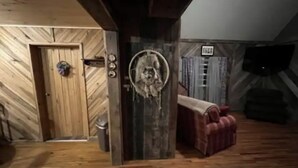 A rustic room with wooden walls, a wooden door, a red sofa, and a circular mirror on the wall. - Rustic 1 BR, Pet Friendly Cabin Near Red River Gorge (Campton)