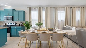 Une cuisine moderne avec des armoires de couleur turquoise, un four à micro-ondes et une cuisinière. On y trouve également un coin repas avec une table dressée pour quatre personnes, des chaises et un canapé gris.