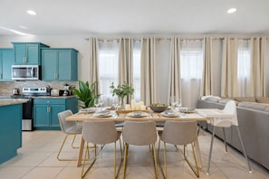 Une cuisine moderne avec des armoires de couleur turquoise, un four à micro-ondes et une cuisinière. On y trouve également un coin repas avec une table dressée pour quatre personnes, des chaises et un canapé gris.
