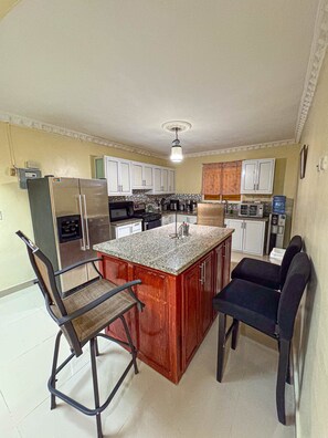 A compact kitchen with a central island, white cabinets, and a stainless steel refrigerator.