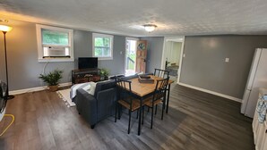 Uma sala de estar moderna com um sofá cinzento, mesa de jantar de madeira e uma TV sobre um móvel.